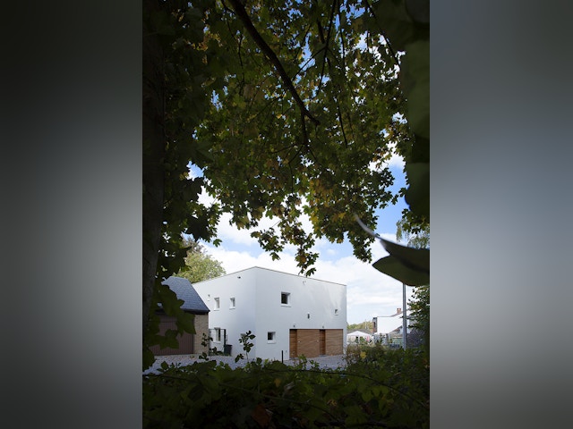 Ce cube compact abrite sans en avoir l’air deux logements symétriques. Pour éviter toute lourdeur, la pureté de la forme cubique est animée de percements aléatoires.