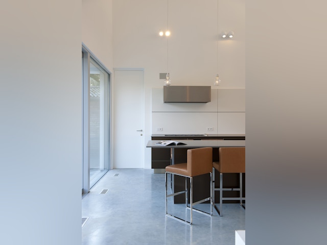 Dans la cuisine, la haute porte vers le garage et les luminaires suspendus au-dessus de l’îlot cassent le sentiment de trop grande hauteur.
Toute la maison est chauffée à l’air chaud, soufflé dans la pièce par des grilles encastrées dans le sol.